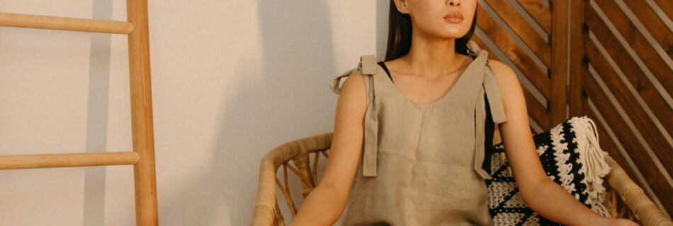 Mujer sentada en postura de loto sobre una silla de mimbre, con los ojos cerrados, en un ambiente tranquilo que evoca paz y meditación. Ideal para artículos sobre bienestar, mindfulness y relajación.