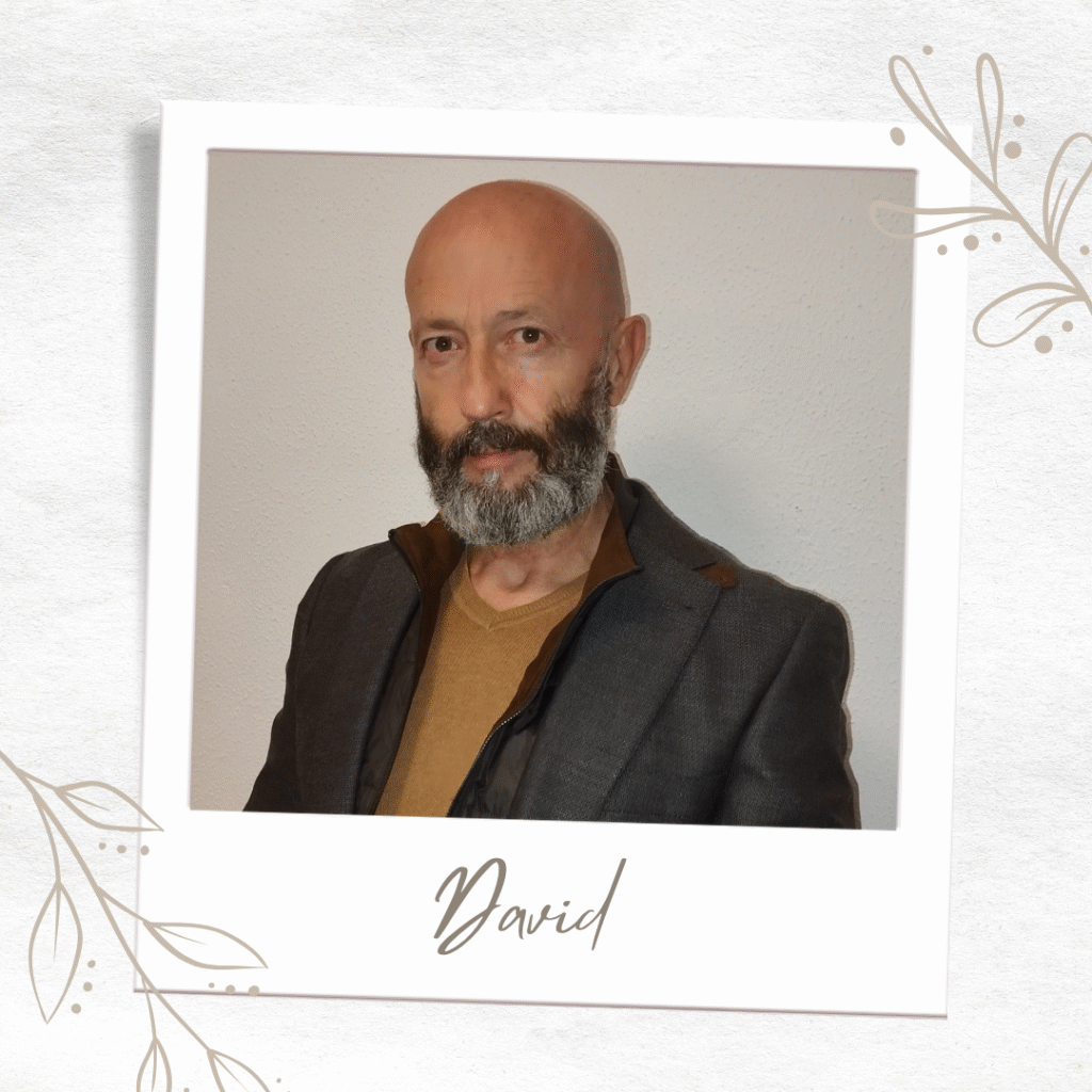 Retrato formal de David Sánchez, guía espiritual con más de 15 años de experiencia en Tarot y Numerología. Se presenta en un encuadre tipo fotografía polaroid con diseño floral minimalista, viste una chaqueta gris oscura sobre un jersey color mostaza. Tiene barba gris y es calvo. Su nombre 'David' aparece escrito debajo de su foto.