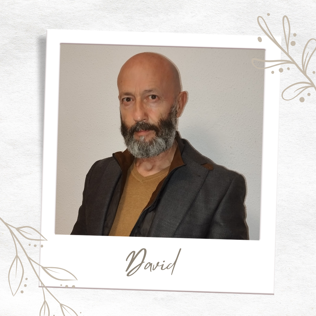 Retrato formal de David Sánchez, guía espiritual con más de 15 años de experiencia en Tarot y Numerología. Se presenta en un encuadre tipo fotografía polaroid con diseño floral minimalista, viste una chaqueta gris oscura sobre un jersey color mostaza. Tiene barba gris y es calvo. Su nombre 'David' aparece escrito debajo de su foto.