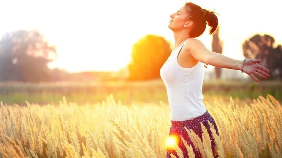 Mujer de perfil con los brazos extendidos hacia el sol en un campo de espigas doradas al atardecer, simbolizando bienestar, libertad, paz y una vida saludable. Imagen que representa la sanación cuántica y la plenitud emocional que se logra con la Nueva Terapia LNT.